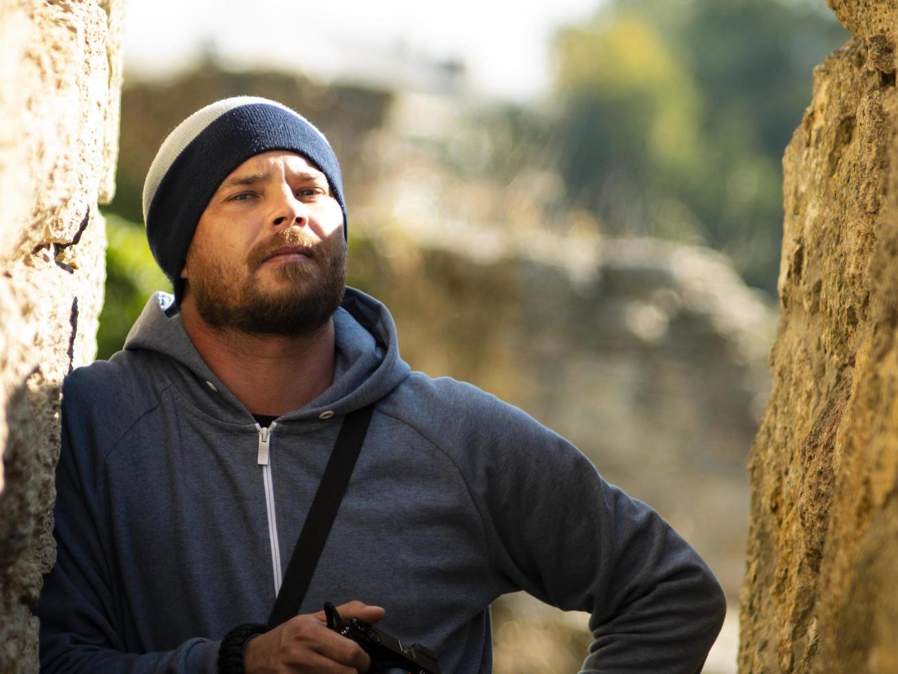 bearded man in jacket with hood posing in a ravine of a fortress photo