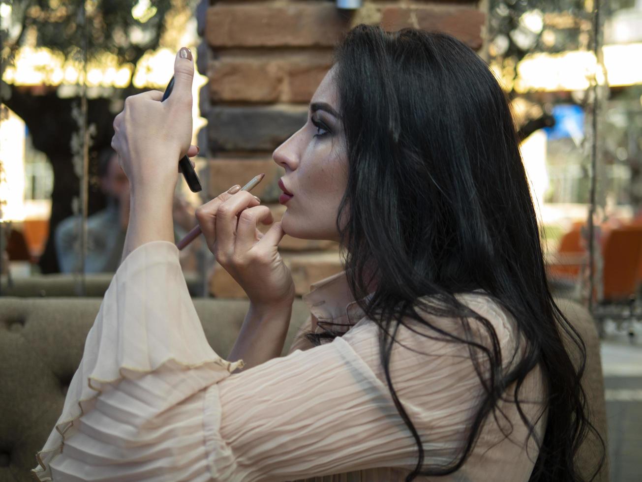 beautiful girl looks in a small mirror and paints her lips photo
