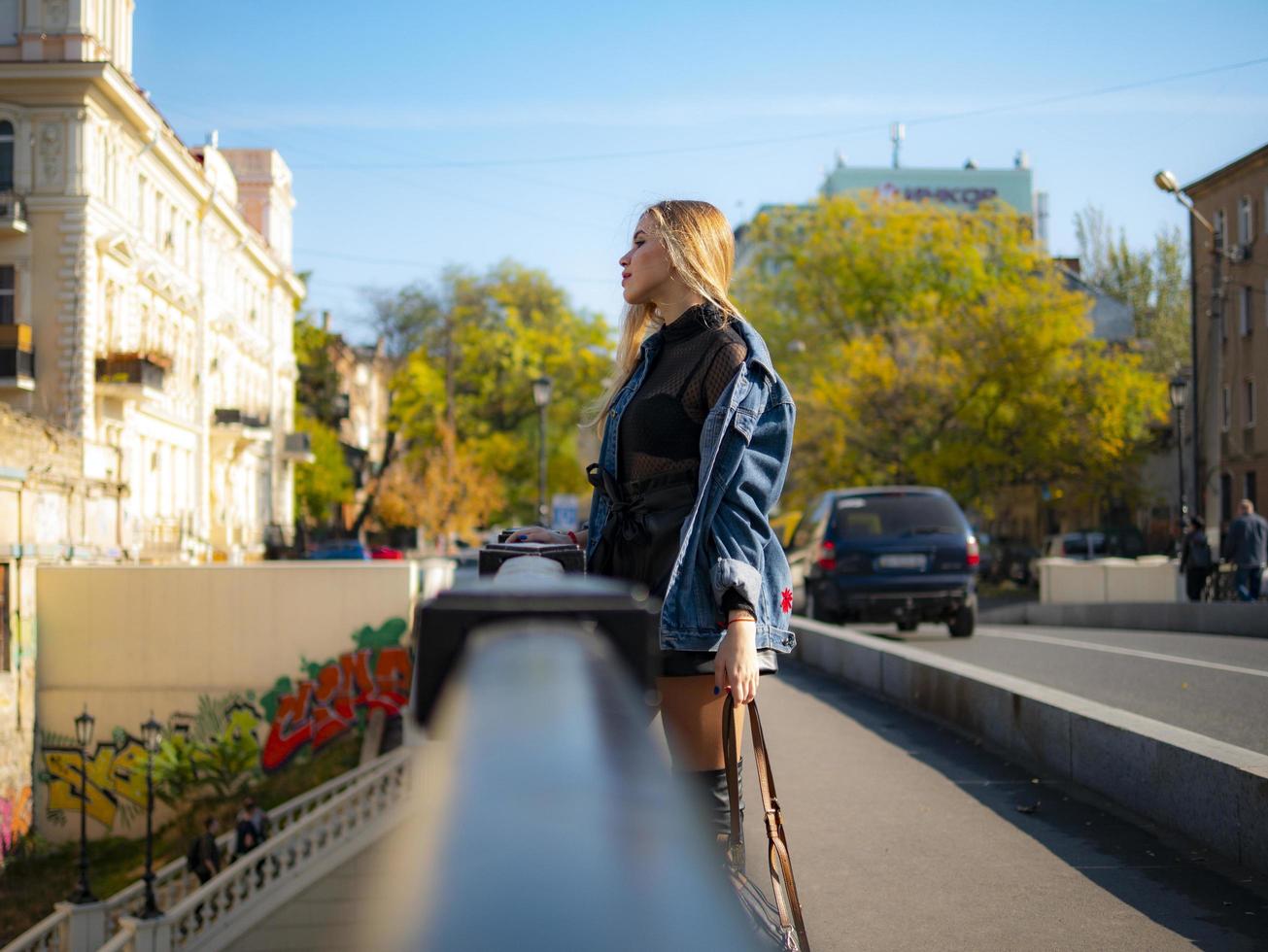 attractive blonde girl in a denim jacket stands on a bridge photo