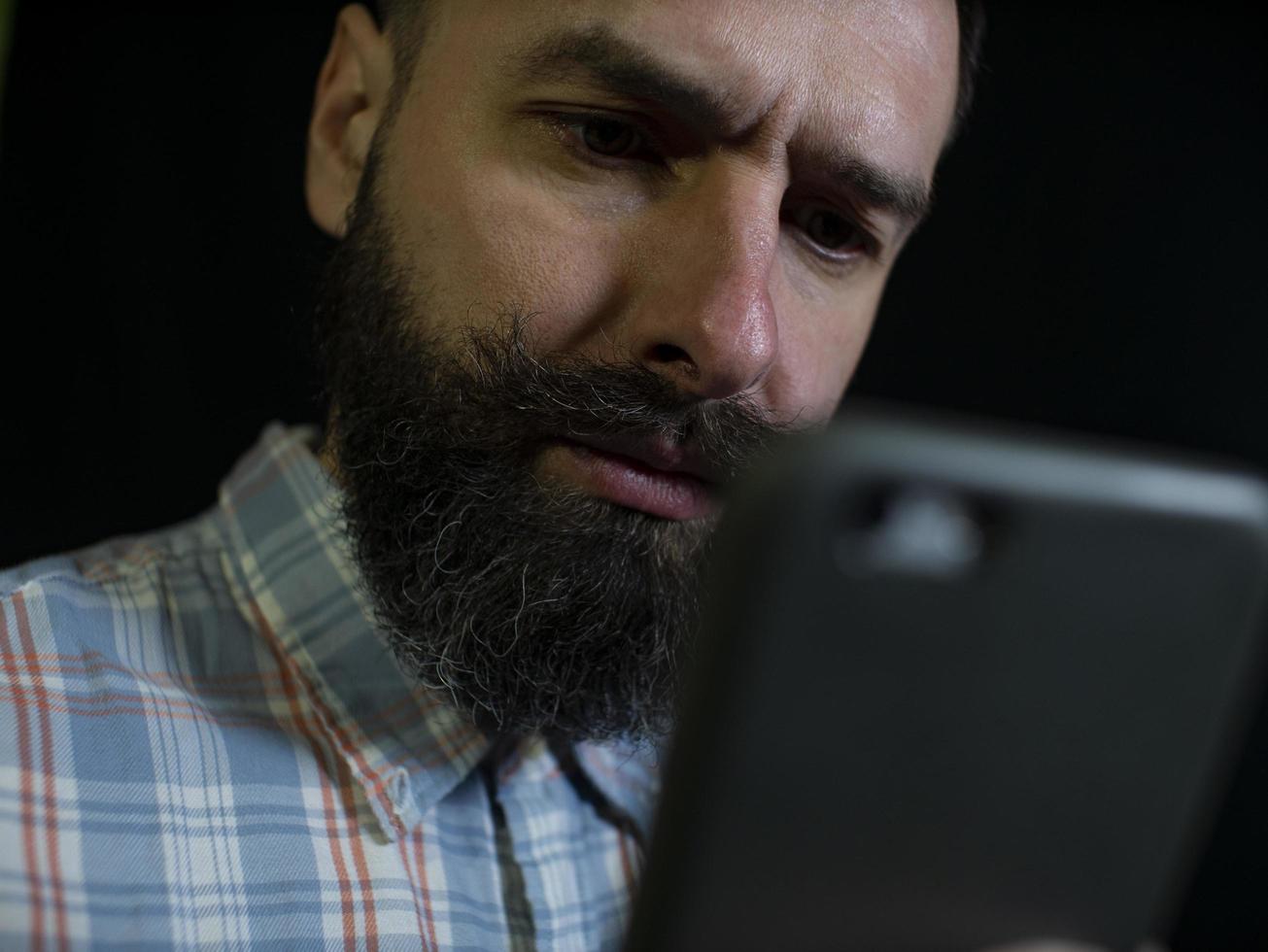 Hombre elegante con barba y bigote mira un teléfono móvil foto