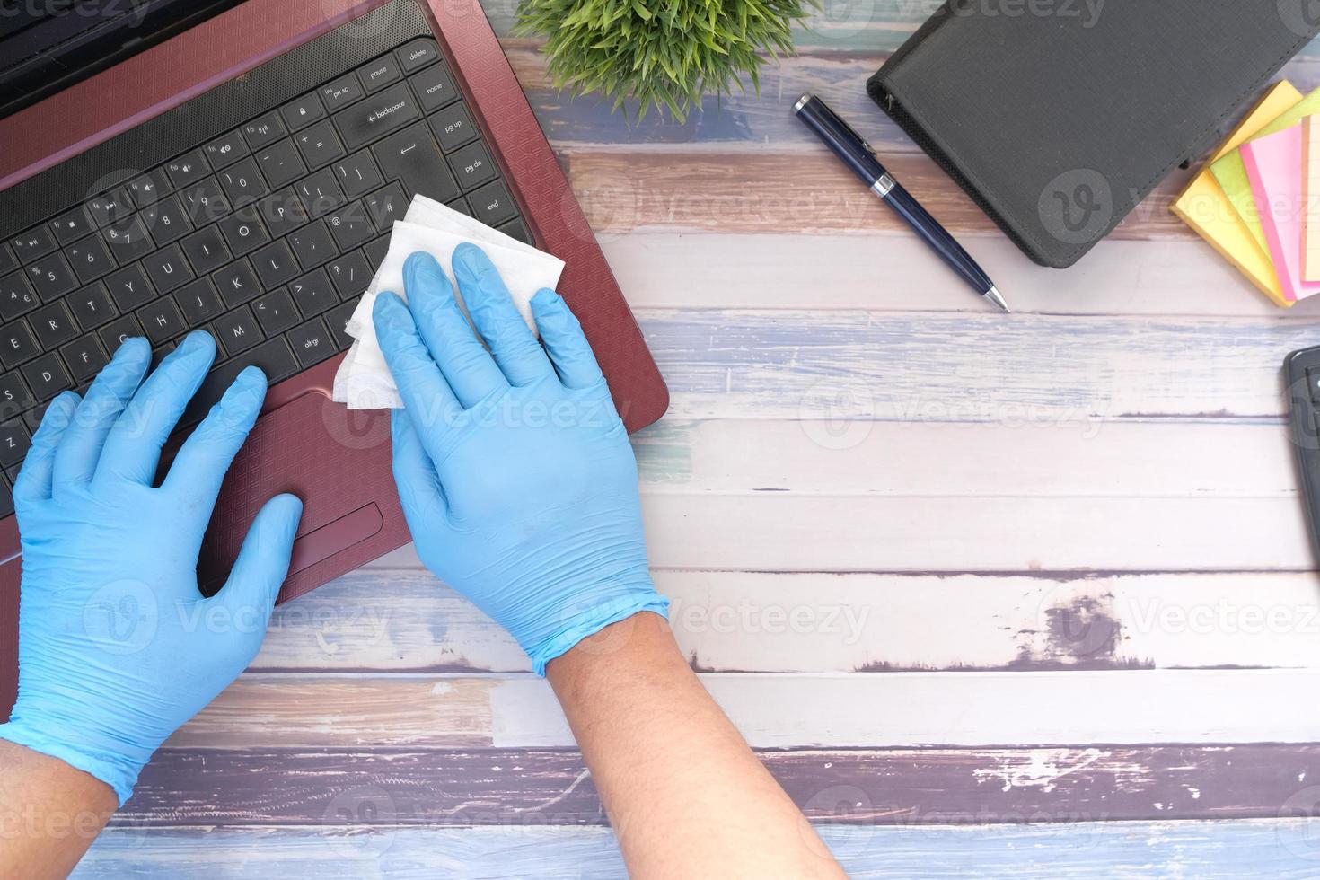 Mano en guantes de goma azul y teclado desinfectante de tejido blanco foto