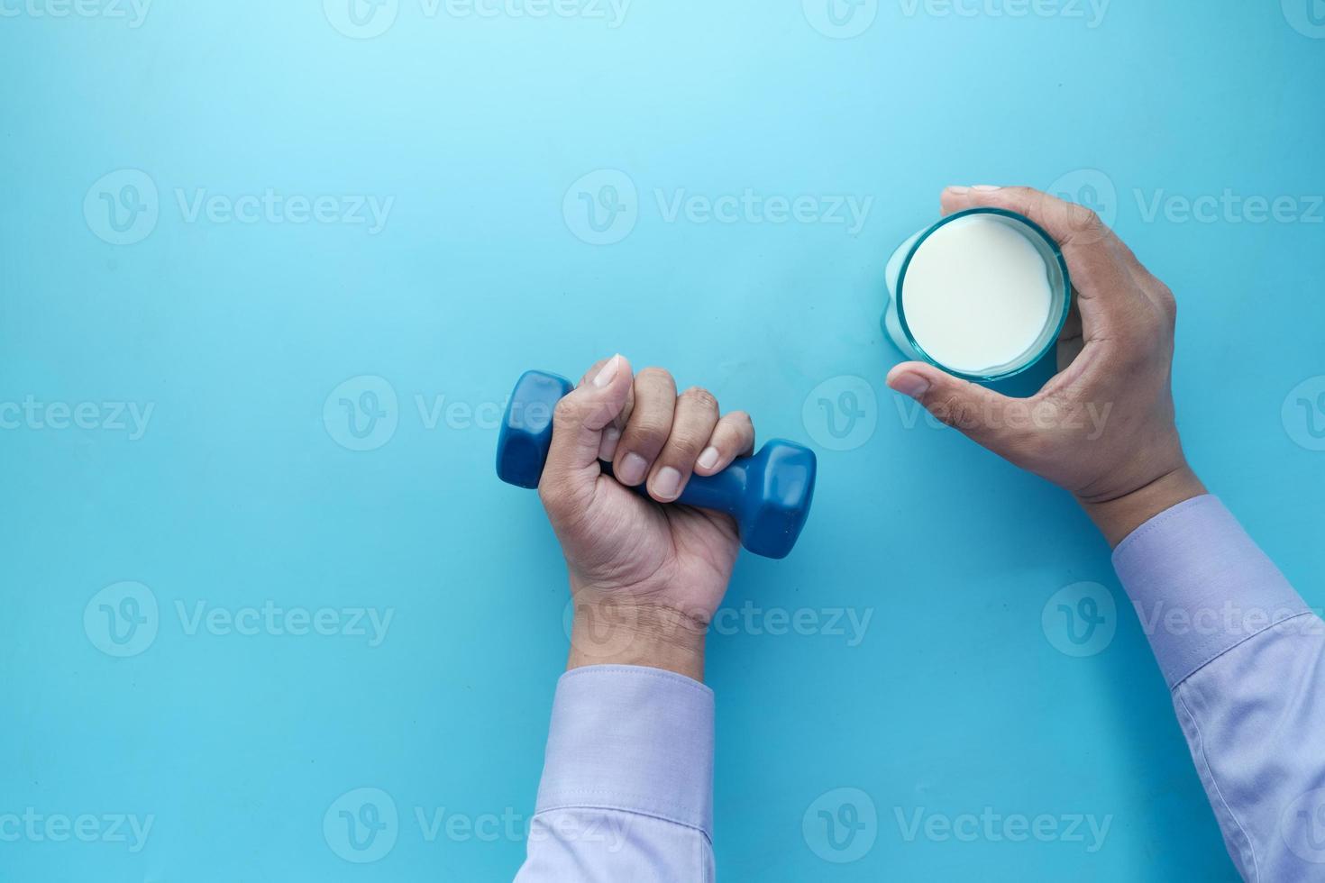 young man hand holding dumbbell and glass of milk on blue photo