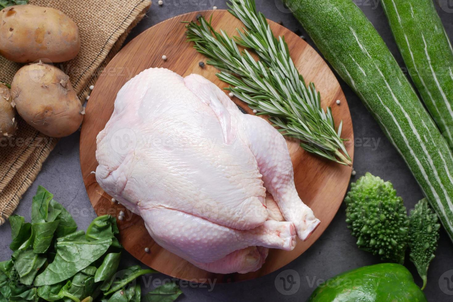 raw whole chicken and green vegetables on table, top view photo