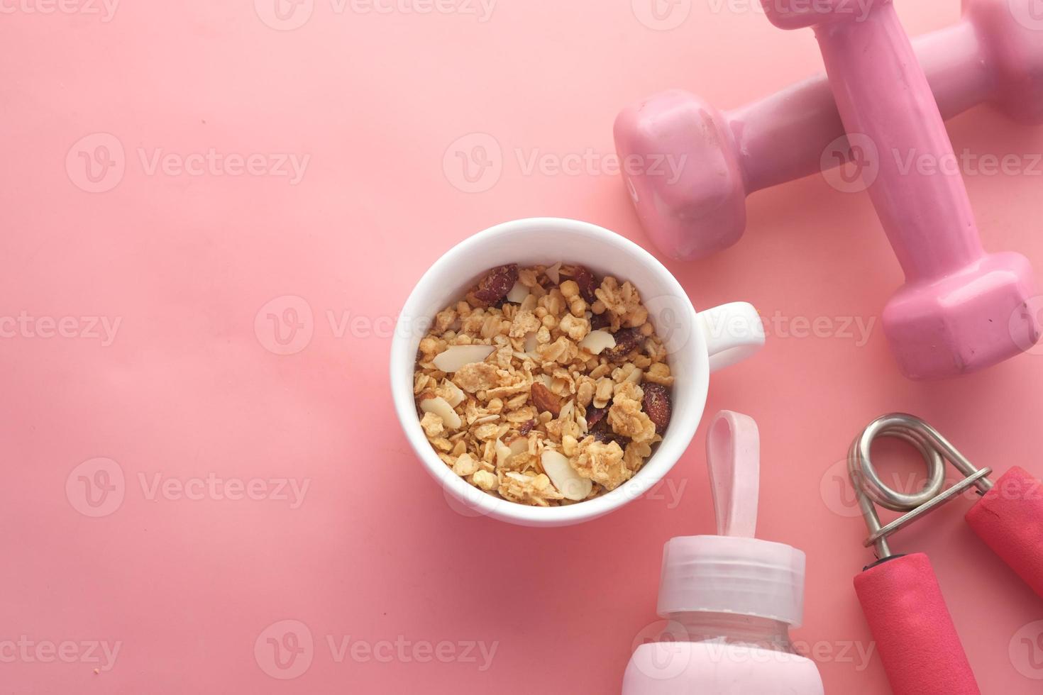 Desayuno de cereales en un tazón y mancuernas de color rosa en la mesa foto