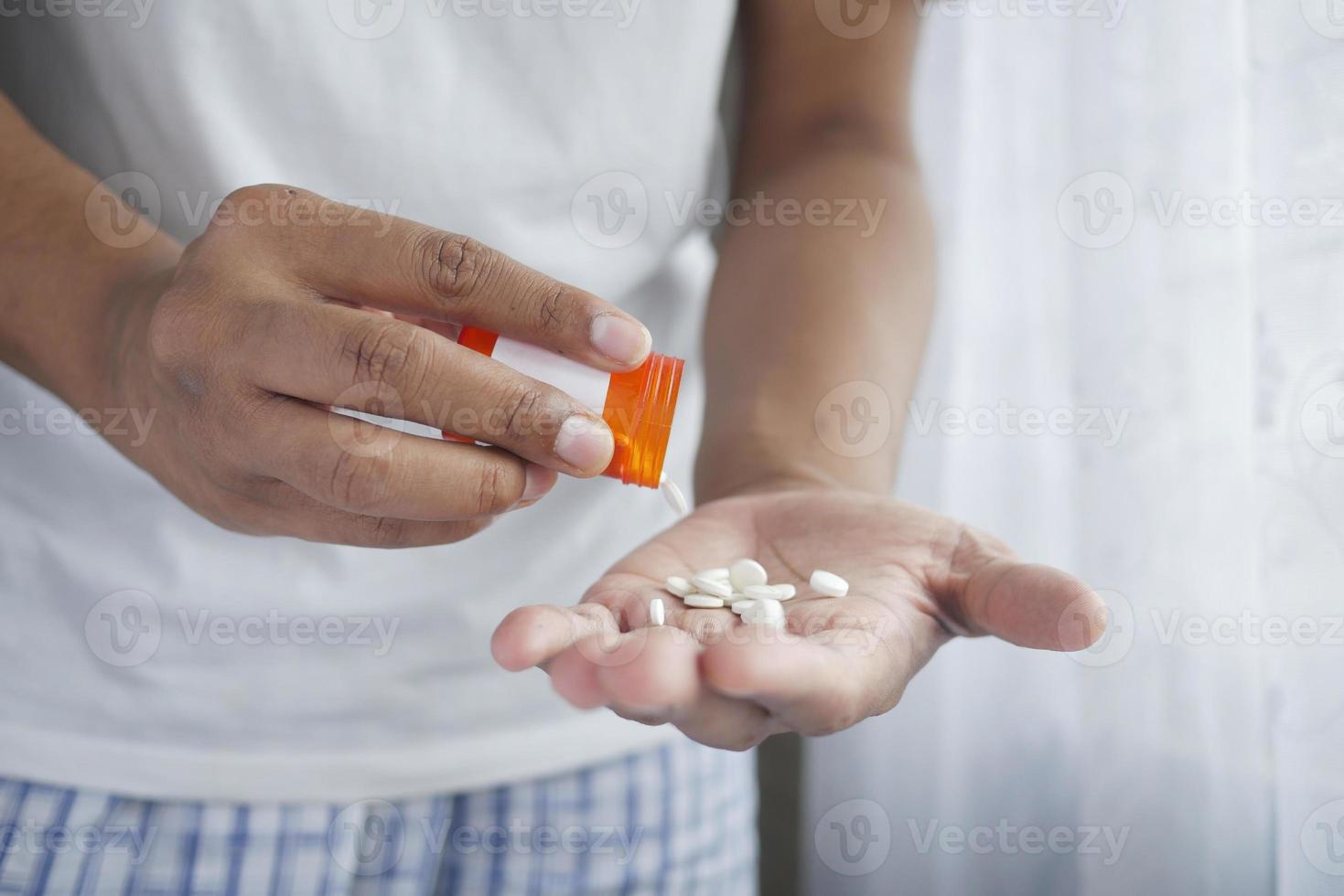 La mano del hombre con la medicina derramada fuera del contenedor de pastillas foto