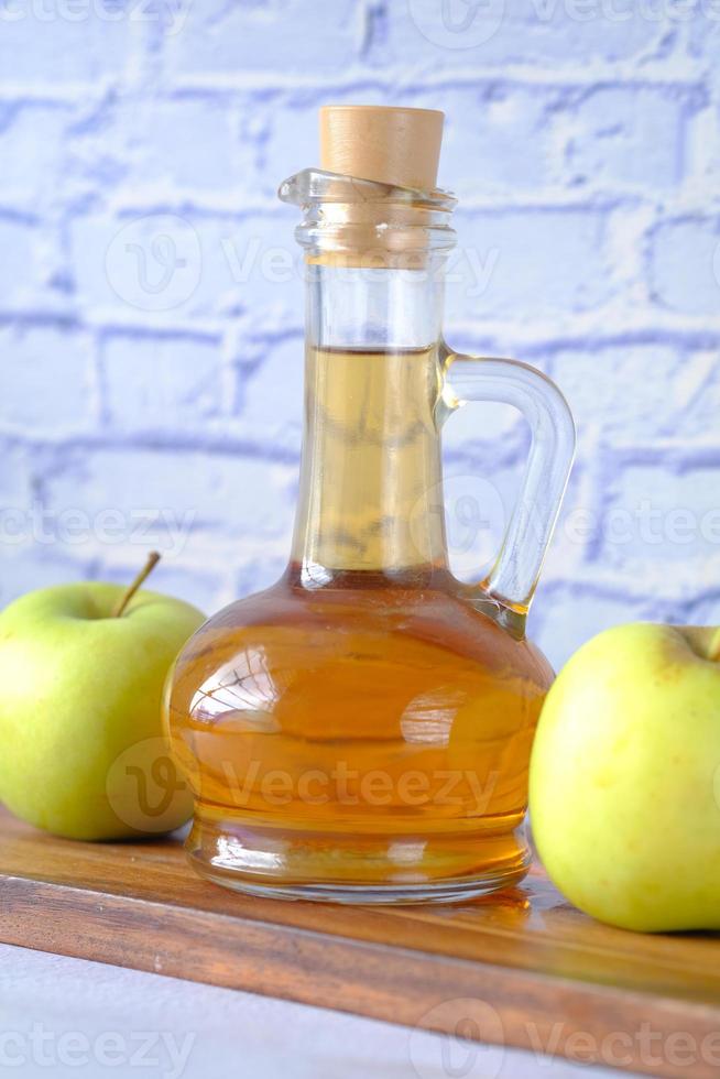 Vinagre de manzana en botella de vidrio con manzana verde fresca en la mesa foto