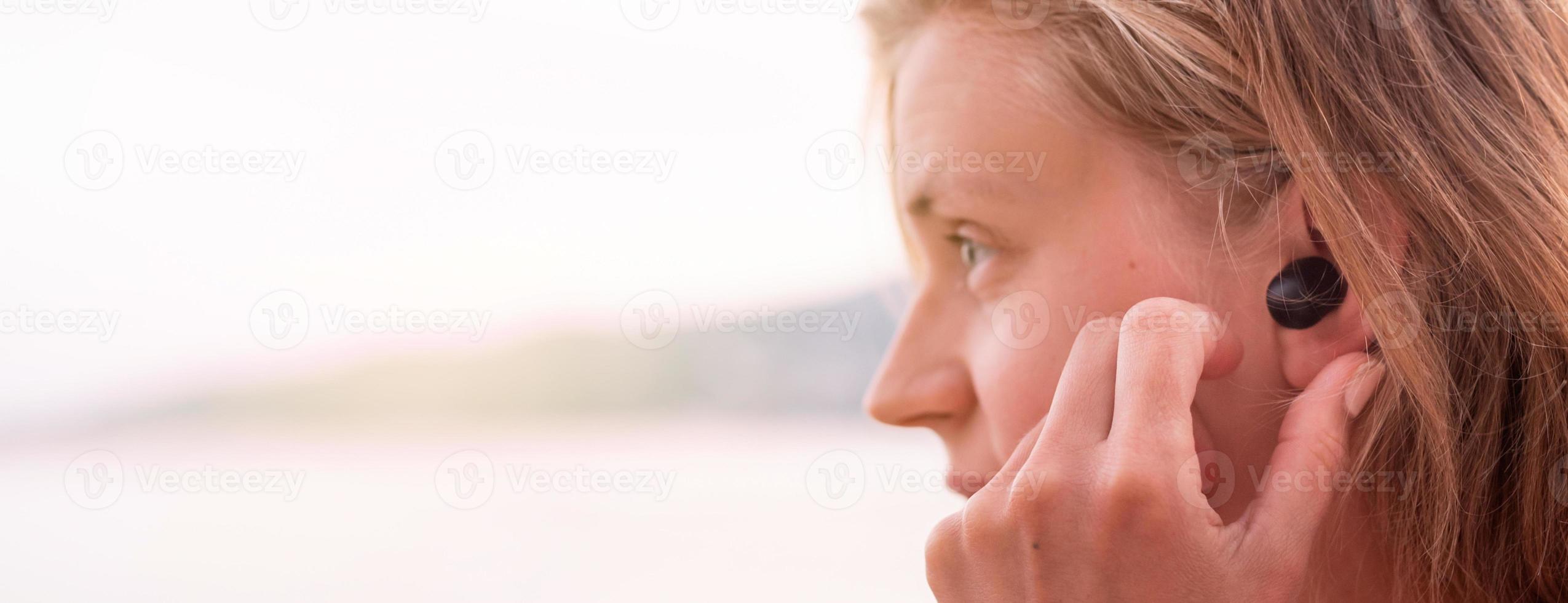 Mujer con auriculares inalámbricos, junto al mar en el fondo foto