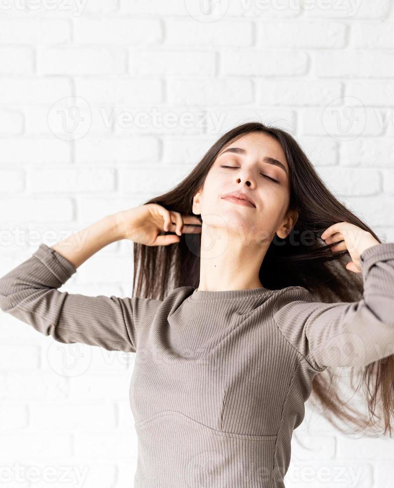 Mujer con cabello largo sobre fondo de pared de ladrillo blanco con los ojos cerrados foto