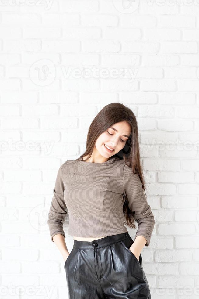 woman on white brick wall background holding hands in pockets photo