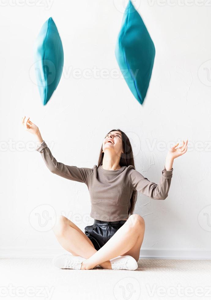 mujer sentada en el suelo tirando almohadas al aire foto