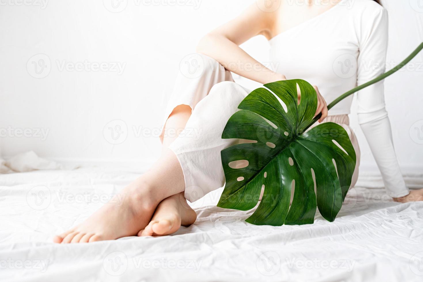 Feliz hermosa mujer en ropa acogedora sosteniendo una hoja de monstera verde foto