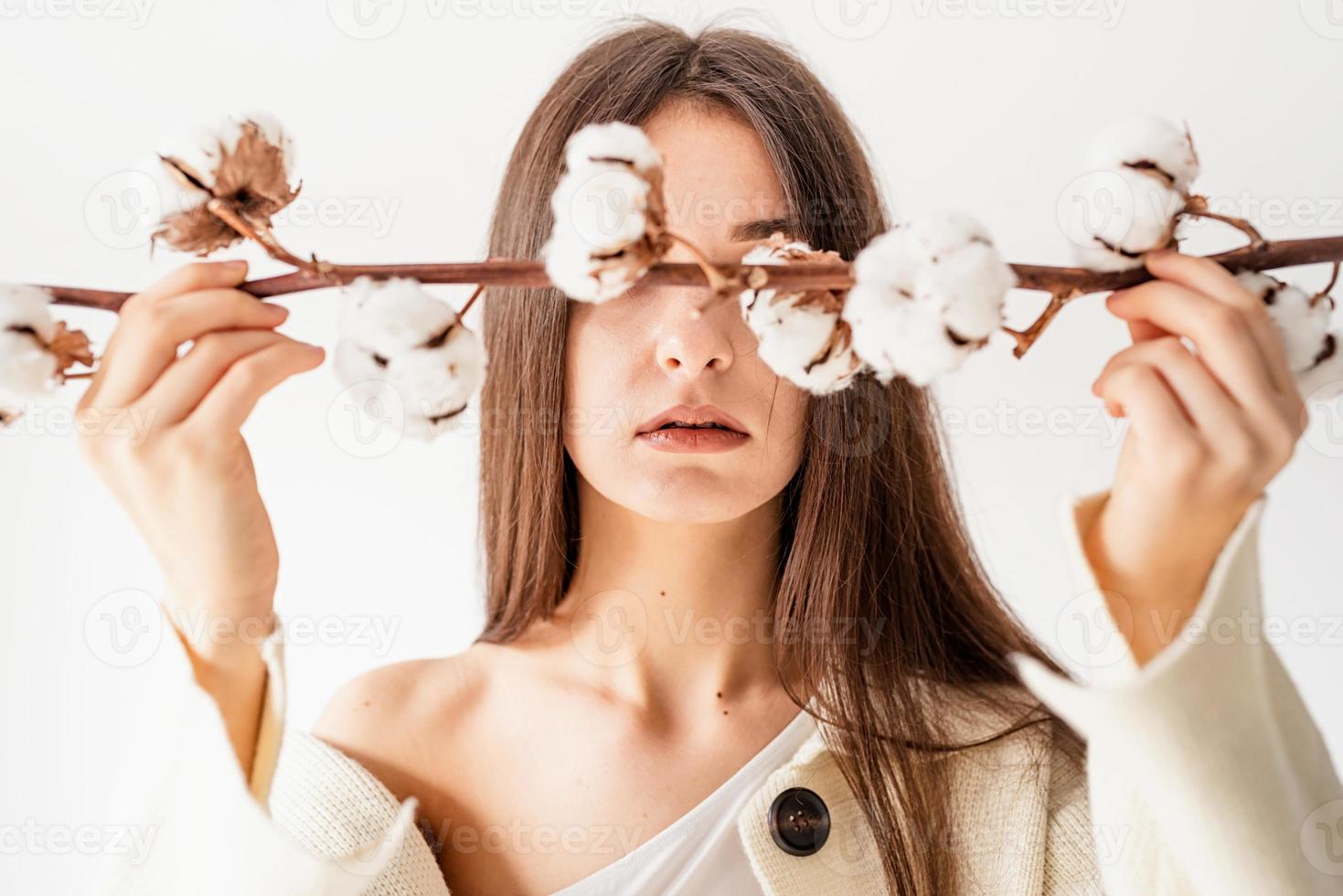 Beautiful woman in cozy clothes holding branch of cotton flowers photo