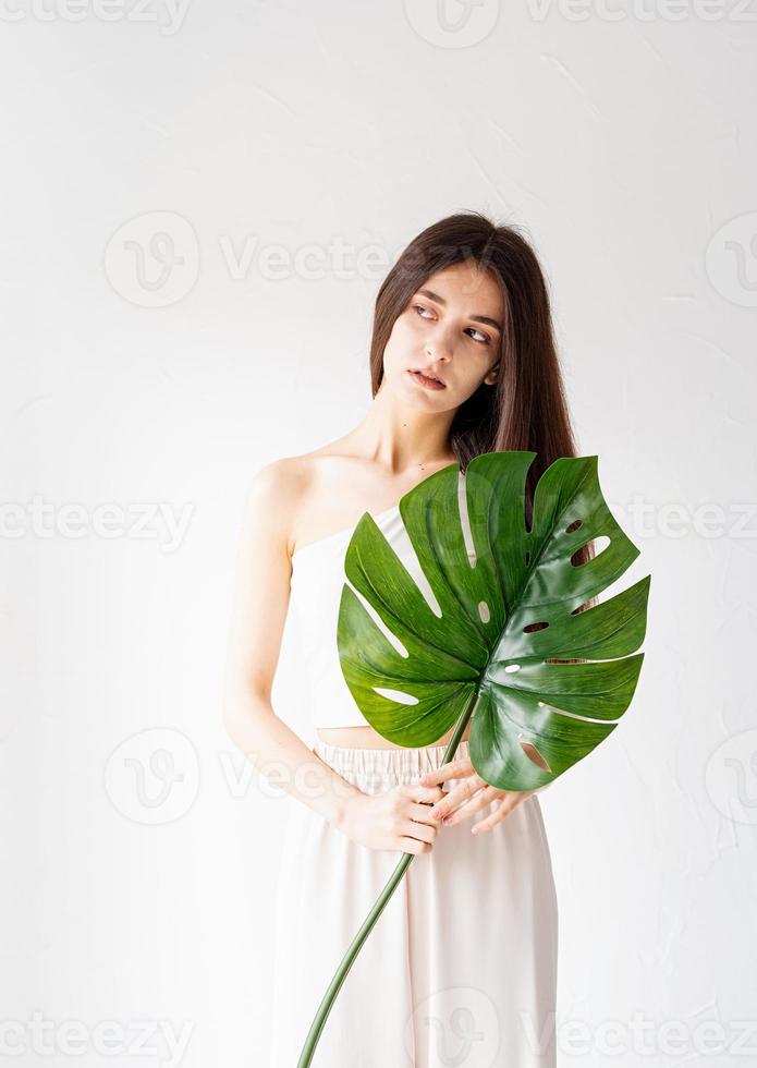 Feliz hermosa mujer en ropa acogedora sosteniendo una hoja de monstera verde foto