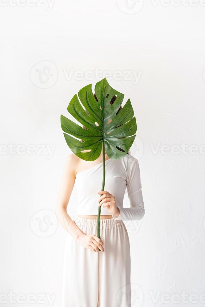 Happy beautiful woman in cozy clothes holding a green monstera leaf photo