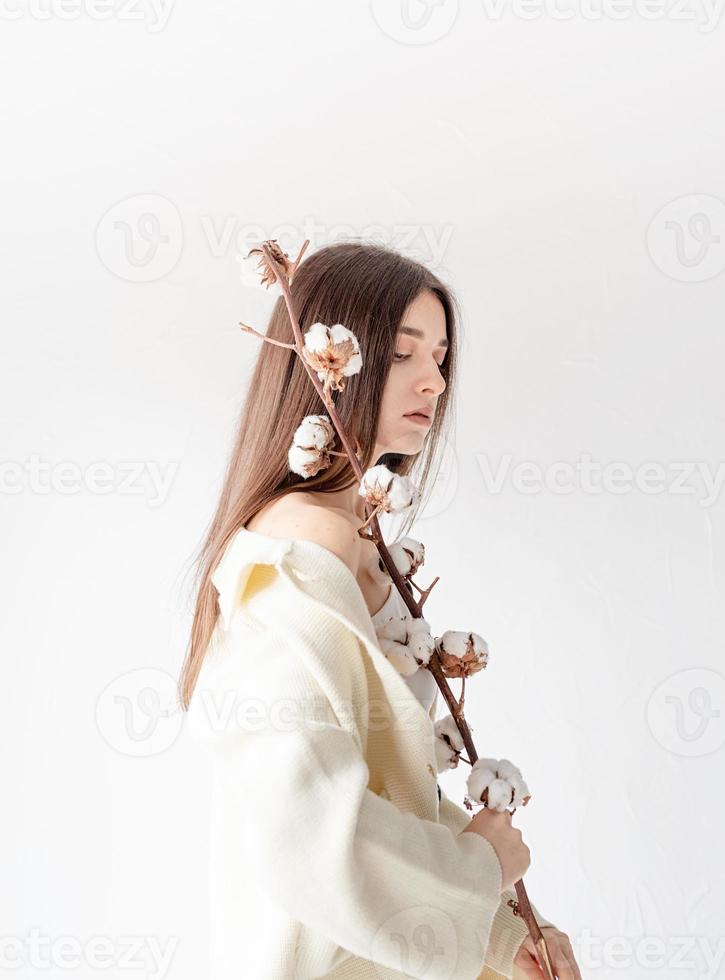 Beautiful woman in cozy clothes holding branch of cotton flowers photo