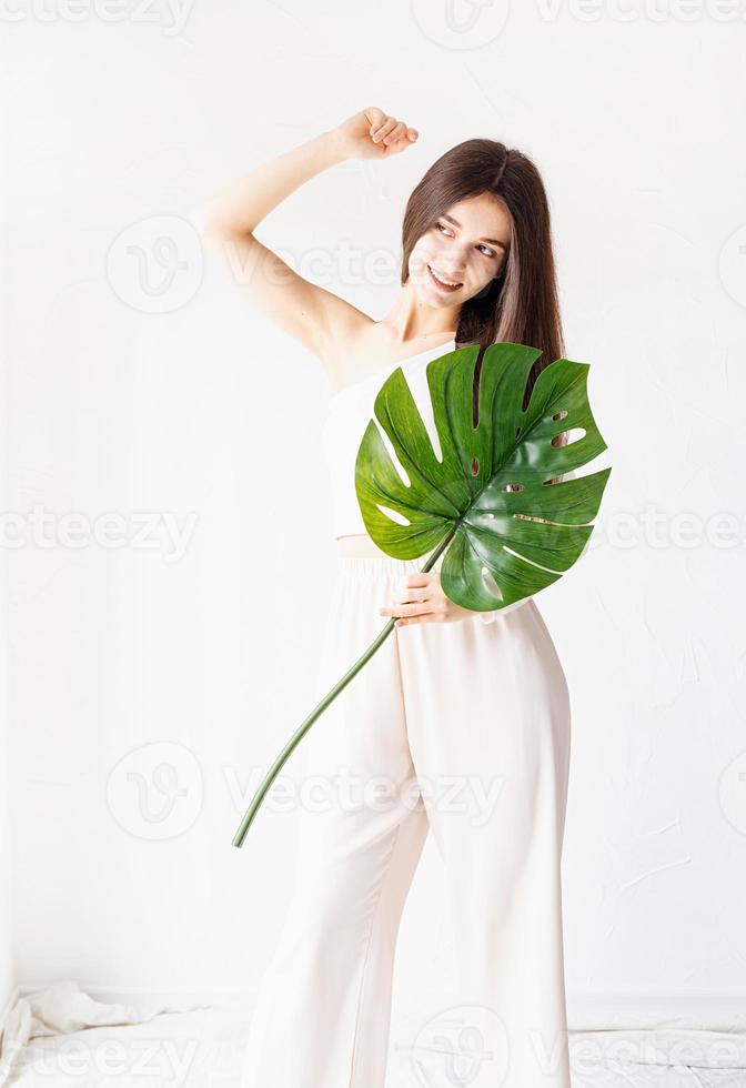 Feliz hermosa mujer en ropa acogedora sosteniendo una hoja de monstera verde foto