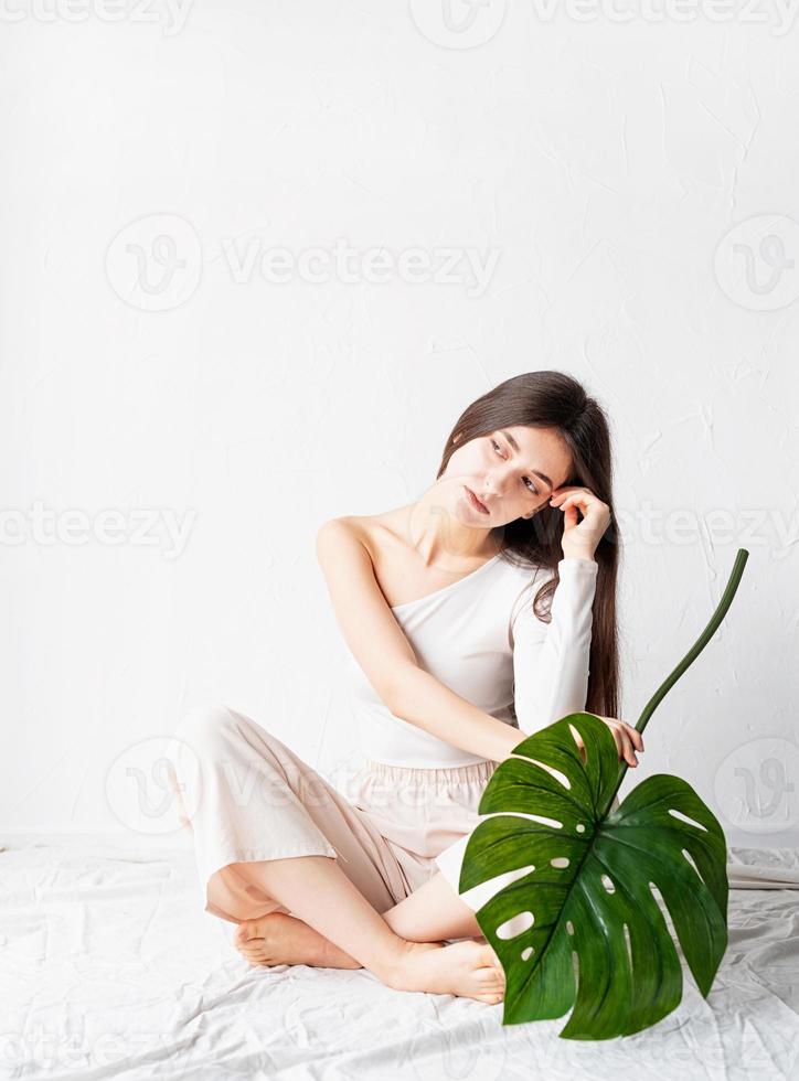 Feliz hermosa mujer en ropa acogedora sosteniendo una hoja de monstera verde foto