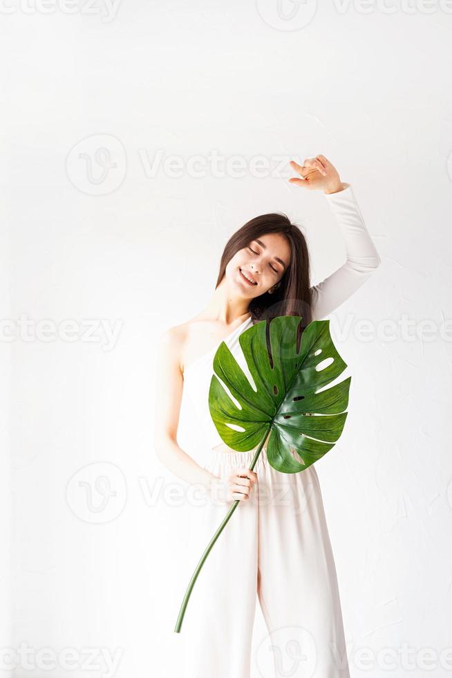 Happy beautiful woman in cozy clothes holding a green monstera leaf photo