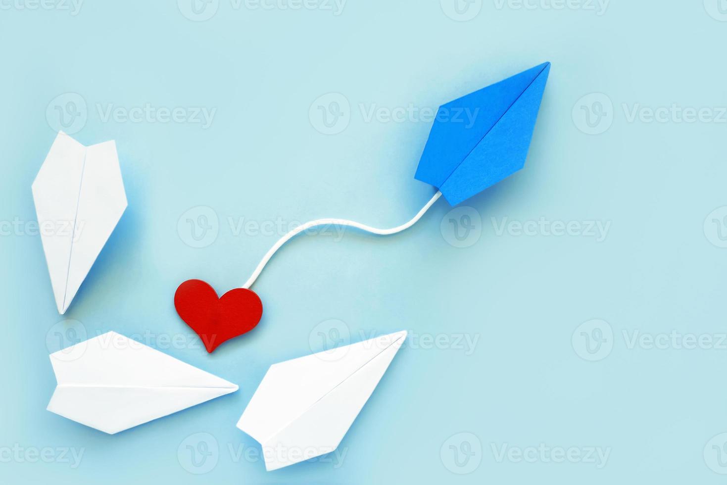 Avión de papel azul con corazón y aviones blancos, sobre fondo azul. foto