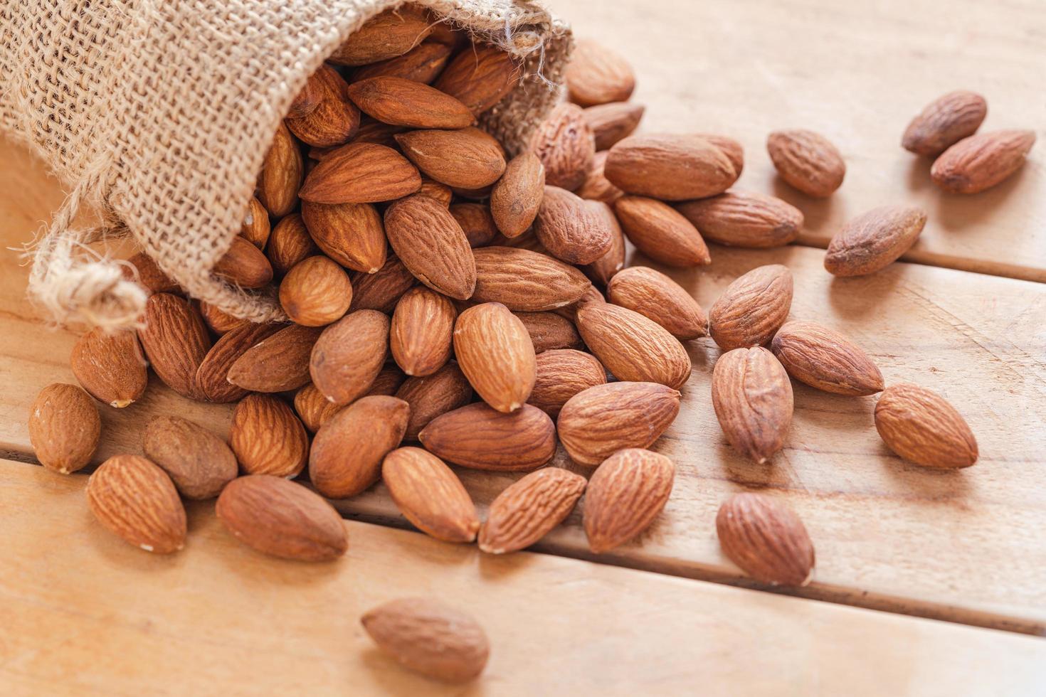 Close up raw peeled almonds seed in sack on wooden background photo