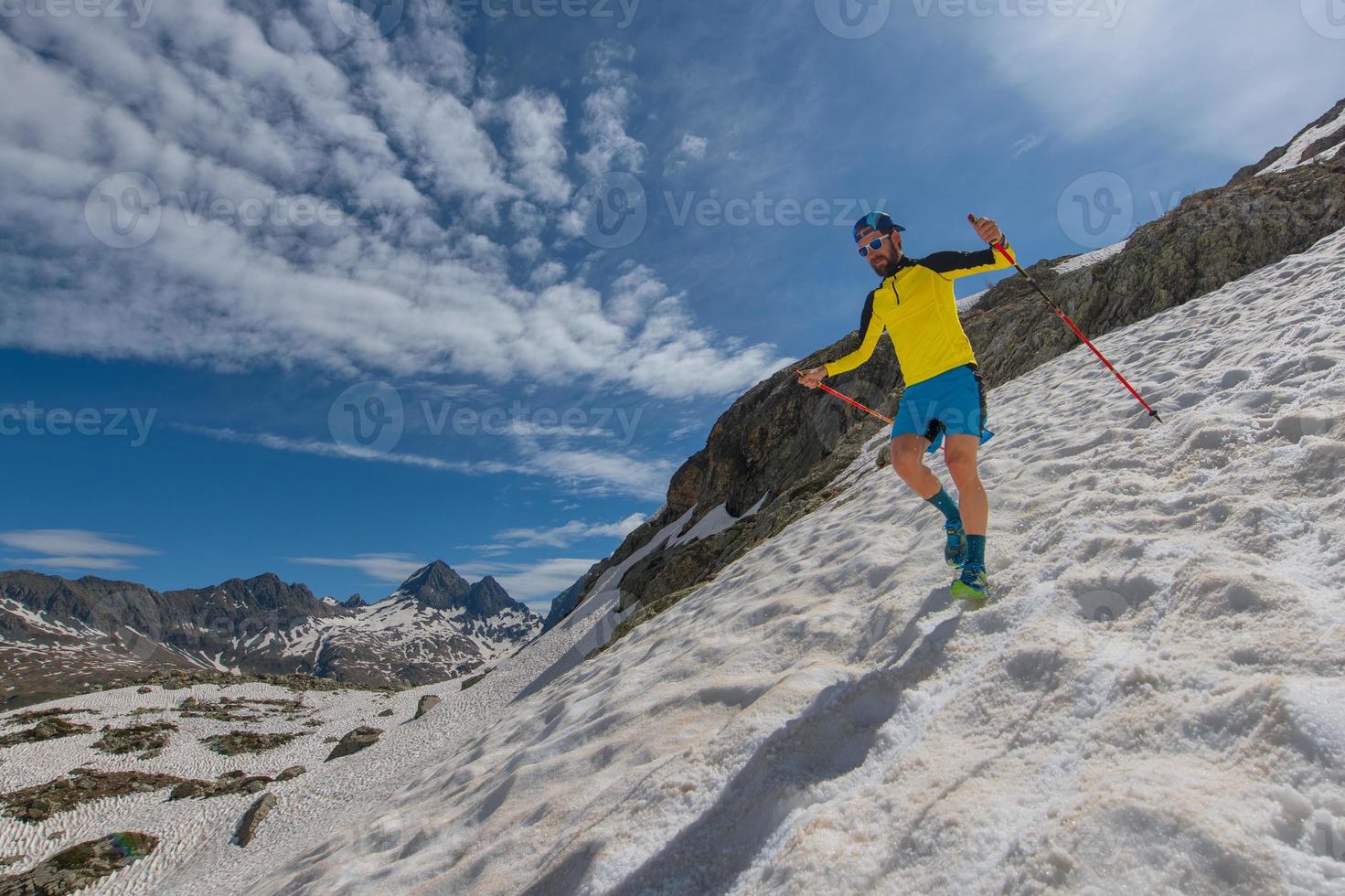 Skyrunner man run downhill on snow between sky and mountains photo