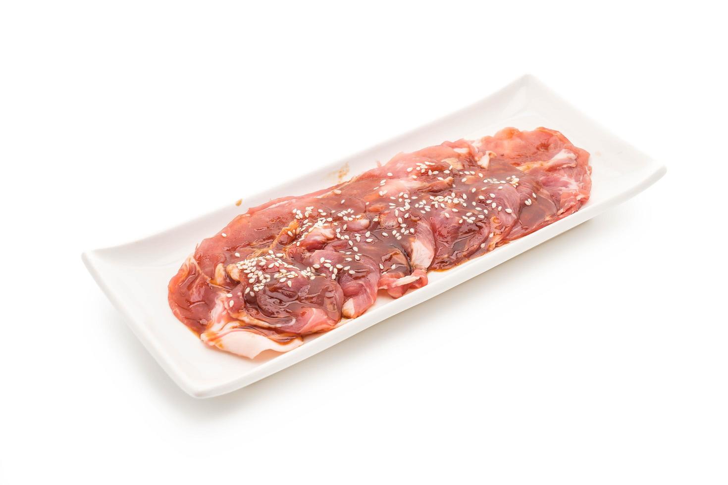 Carne de cerdo fresca en rodajas con salsa y sésamo sobre fondo blanco. foto