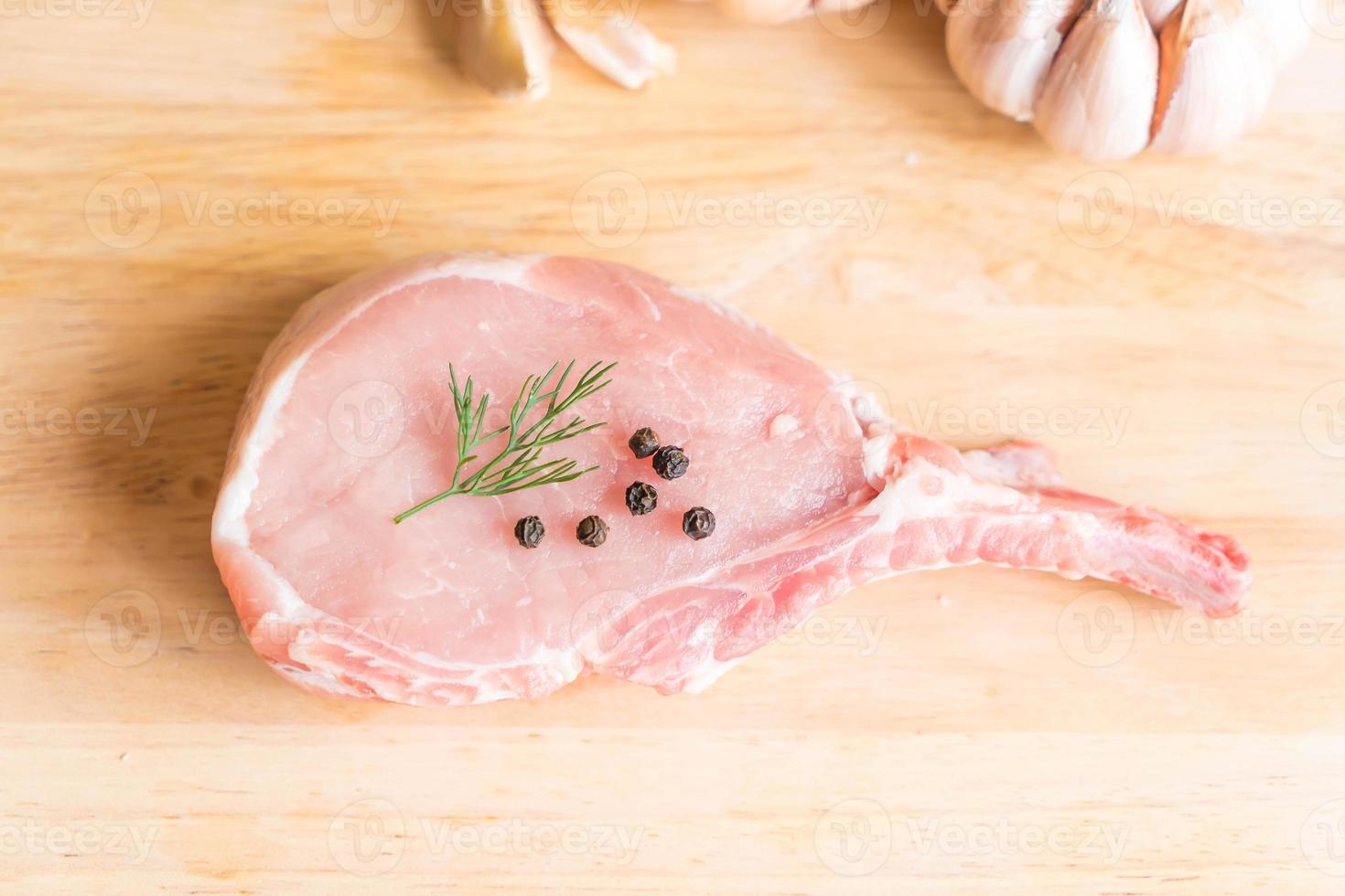 Chuleta de cerdo fresca sobre tablero de madera con ajo y pimientos negros foto