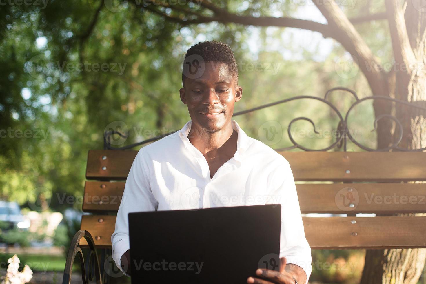 empresario afroamericano, trabajando en una computadora portátil en un banco del parque, foto