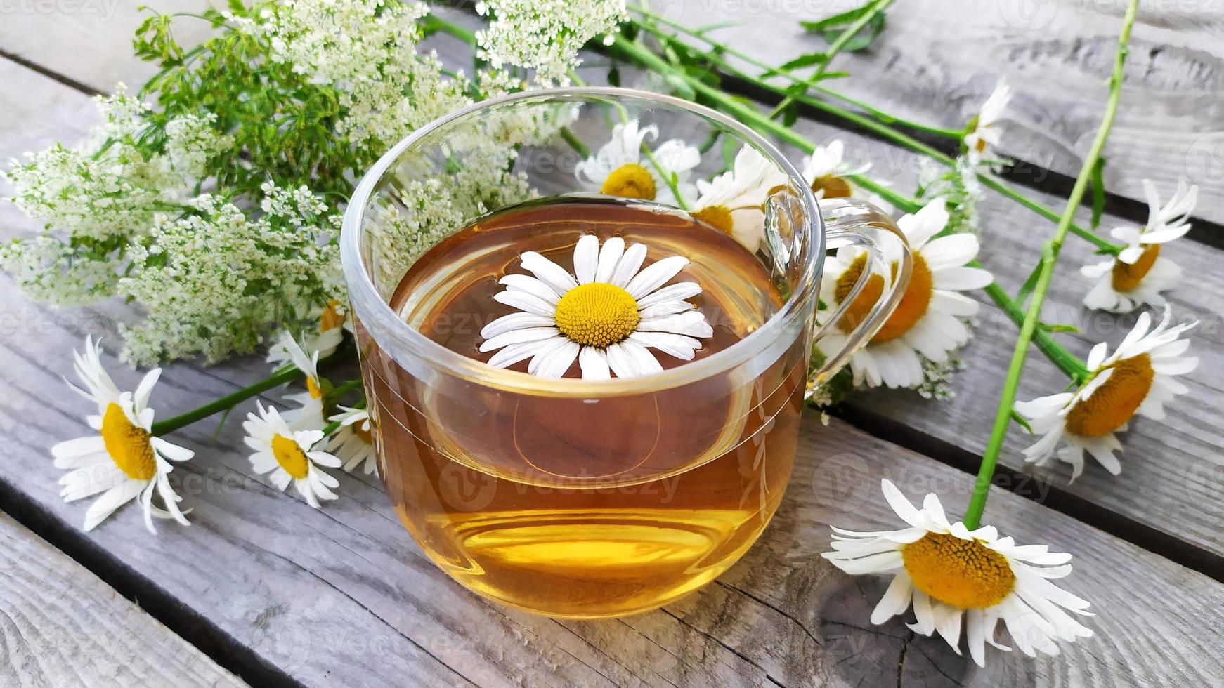 Primer plano de té aromático de manzanilla en una taza de vidrio sobre un fondo de madera. foto