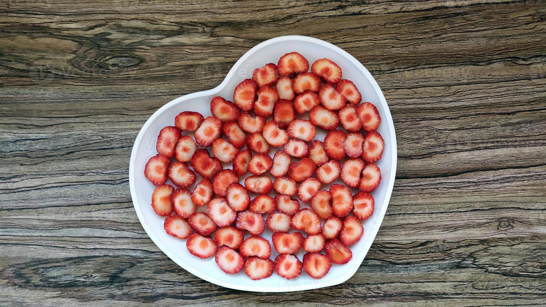 las fresas en rodajas están en un plato en forma de corazón. servicio romántico foto