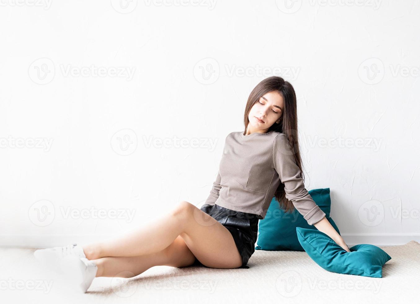 Mujer en ropa casual sentada en el suelo con almohadas foto