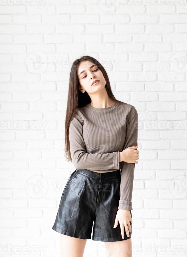 brunette woman with long hair posing on white brick wall background photo