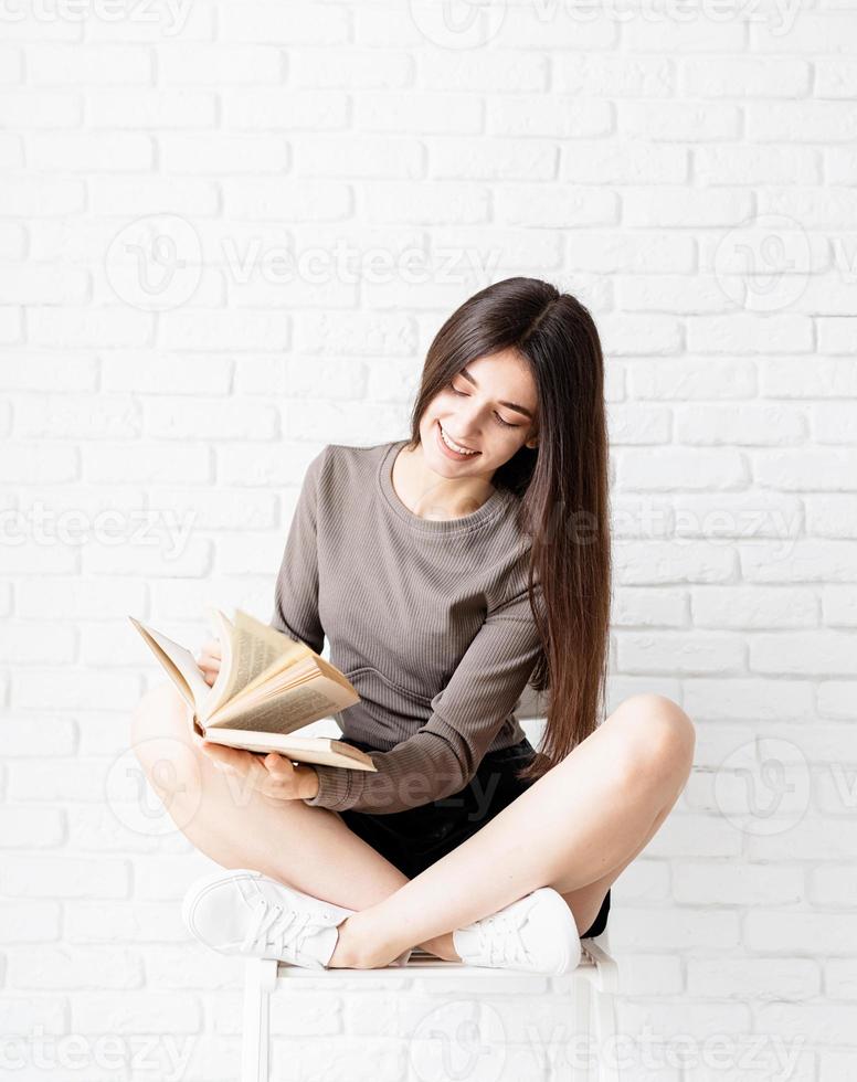 Woman sitting on the chair with legs crossed reading a book photo