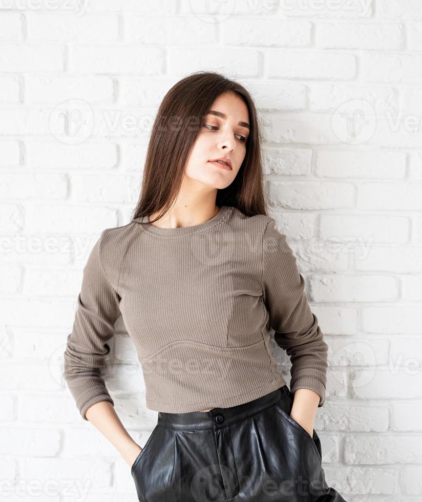 woman on white brick wall background holding hands in pockets photo