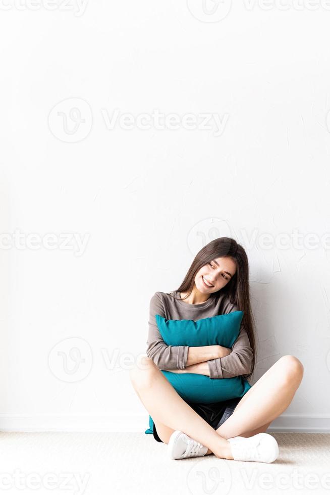 Mujer en ropa casual sentada en el suelo con almohadas sonriendo foto