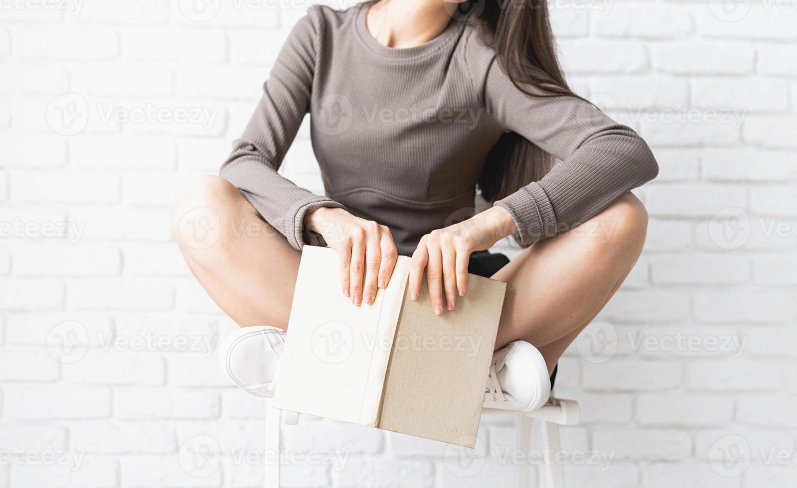 Woman sitting on the chair with legs crossed reading a book photo