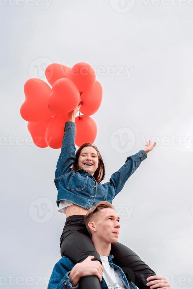 Joven pareja amorosa con globos rojos abrazando al aire libre divirtiéndose foto