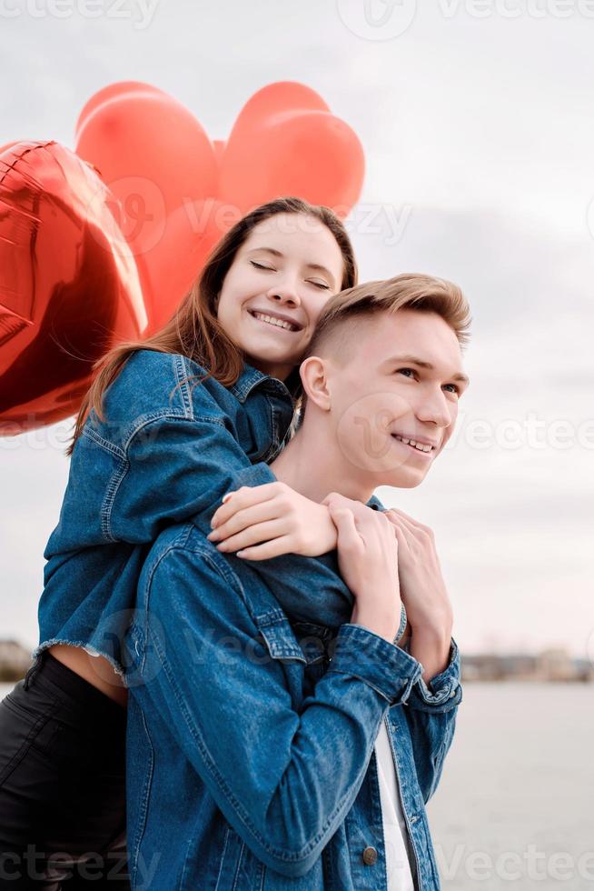 Joven pareja amorosa con globos rojos abrazando al aire libre foto