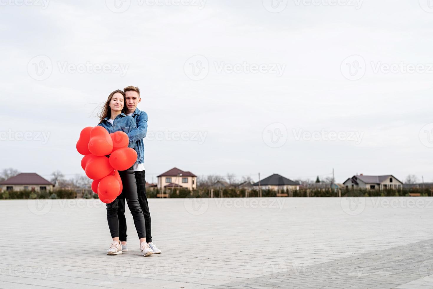 young loving couple with red balloons embracing and kissing outdoors photo