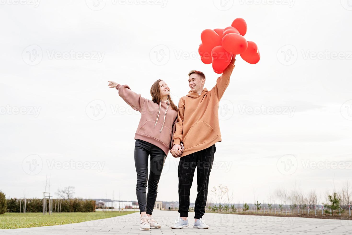 Joven pareja amorosa con globos rojos abrazando al aire libre divirtiéndose foto