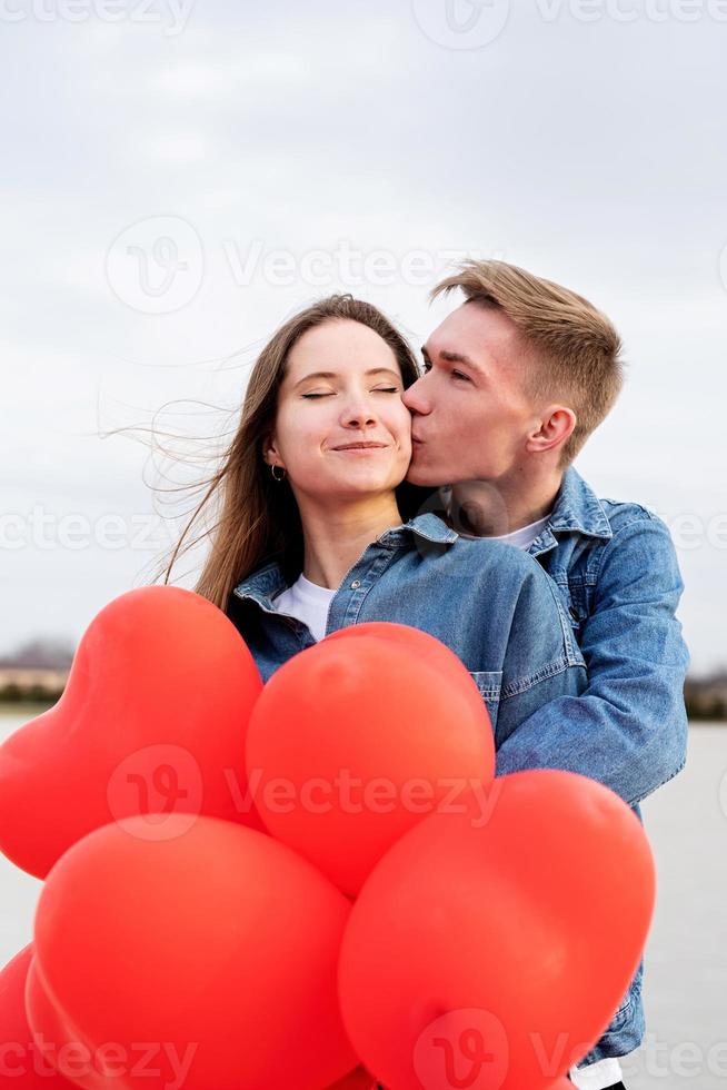 Joven pareja amorosa con globos rojos abrazándose y besándose al aire libre foto