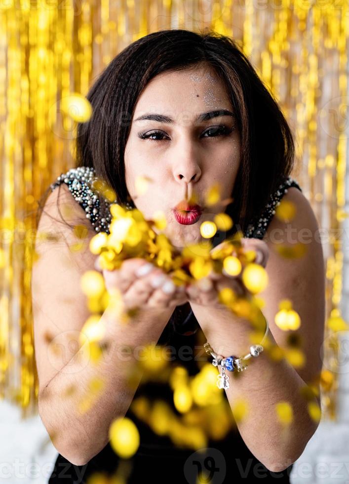 Retrato de hermosa niña soplando confeti dorado en la fiesta navideña foto