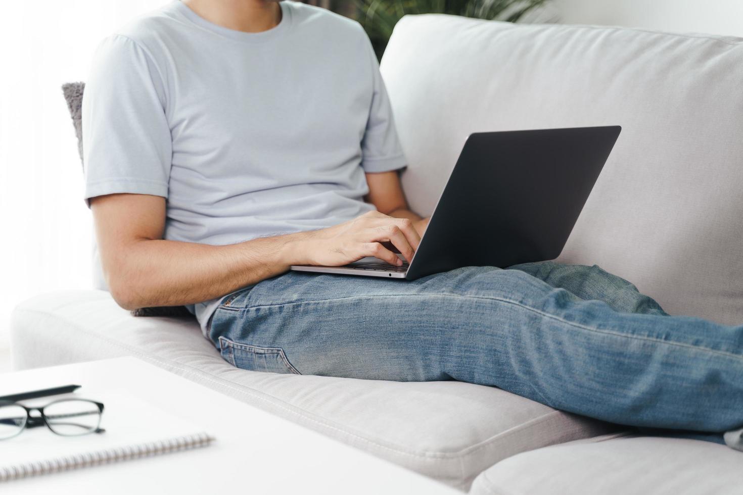 joven sentado en el sofá escribiendo en la computadora portátil para trabajar en línea. foto