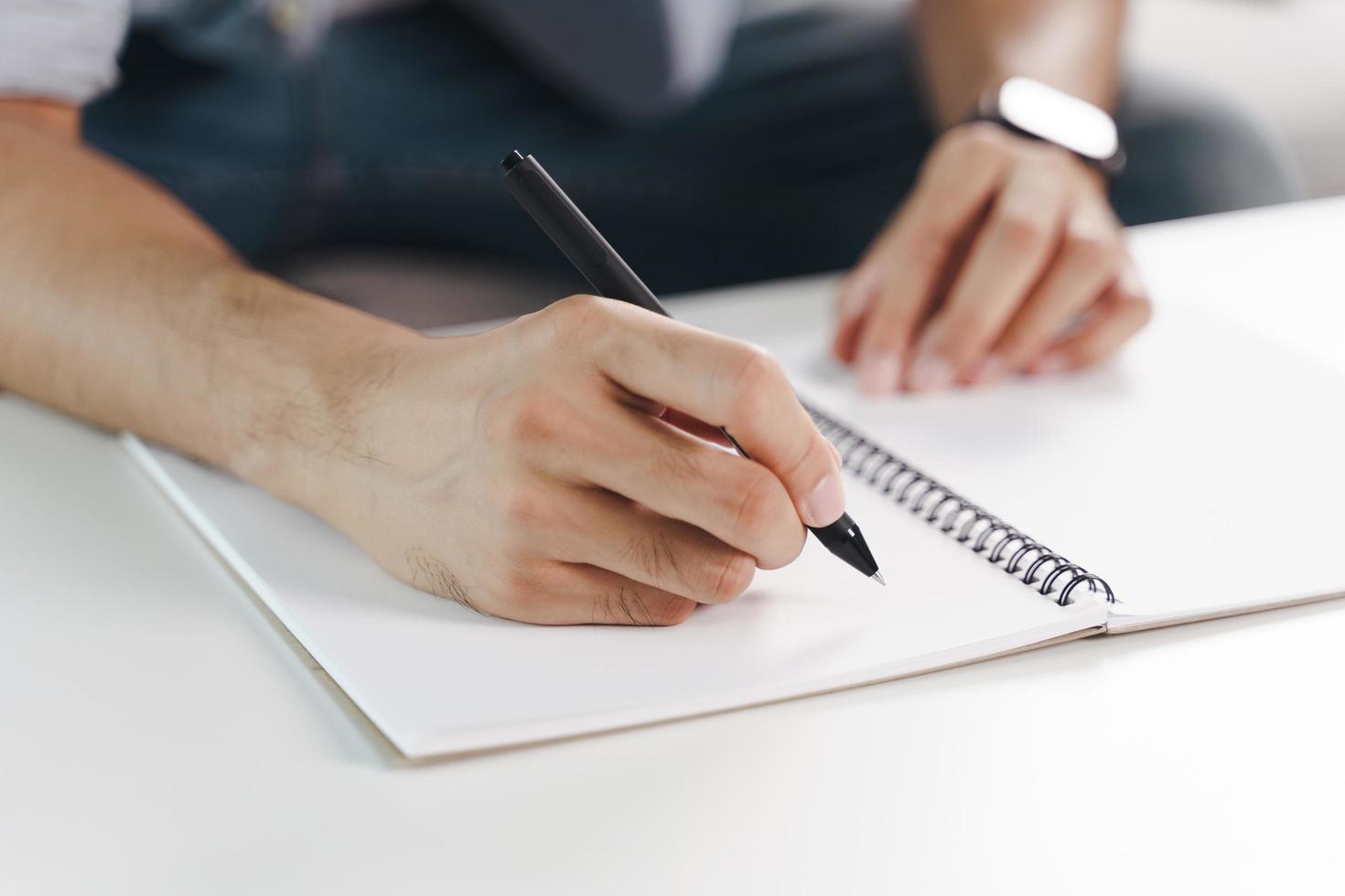 Cerca de las manos del hombre escribiendo en el bloc de notas, cuaderno. foto