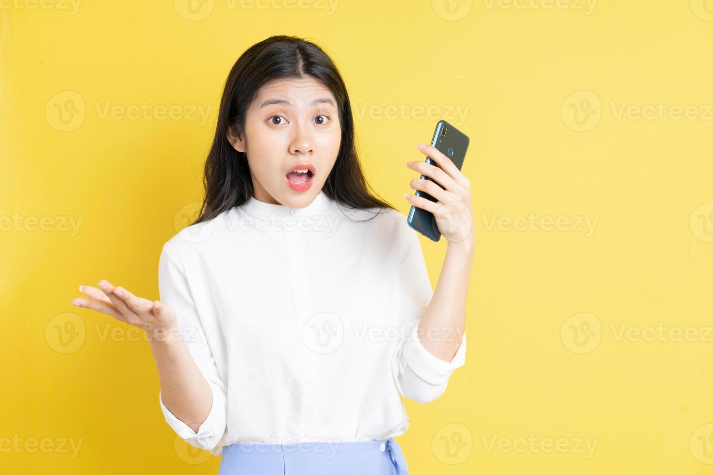 Joven asiática sosteniendo el teléfono con expresión sobre fondo amarillo foto