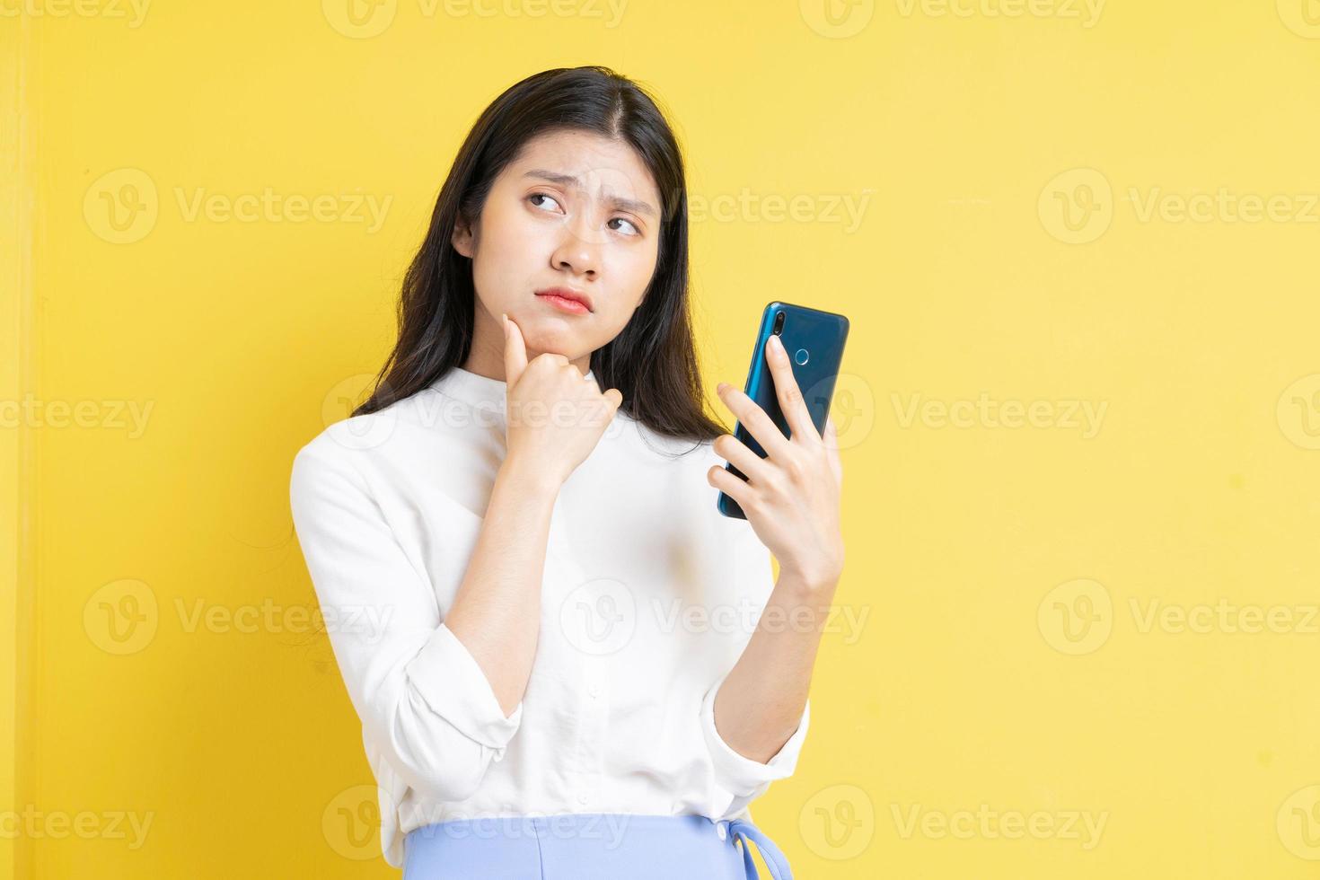Joven asiática sosteniendo el teléfono con expresión sobre fondo amarillo foto