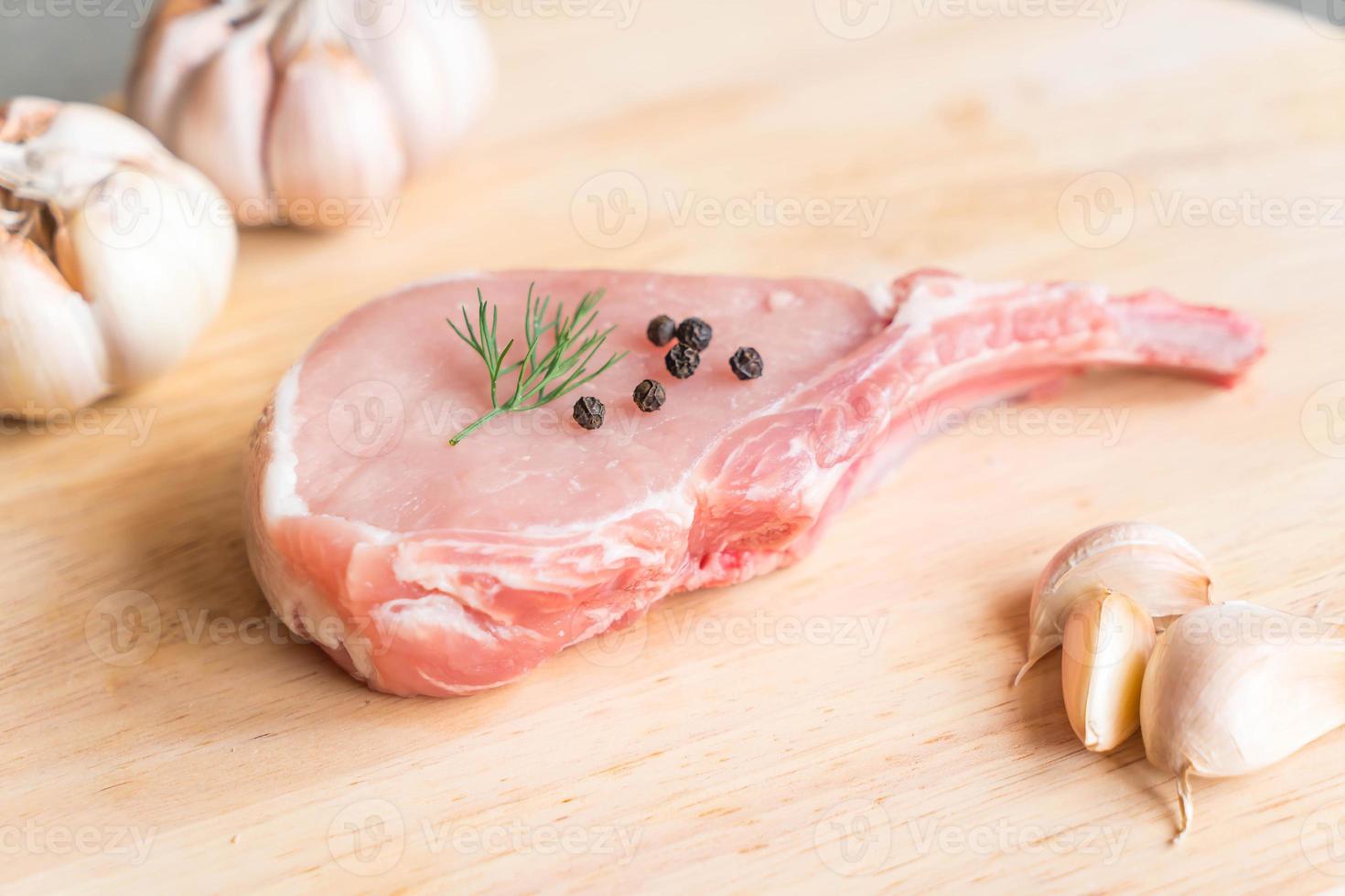 Fresh pork chop on wood board with garlic and black peppers photo