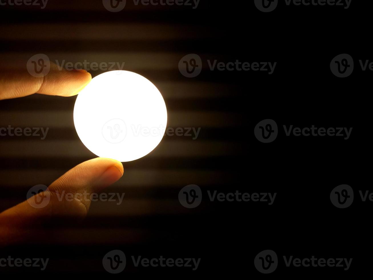 finger holding the lamp that resembles the moon. dark background photo