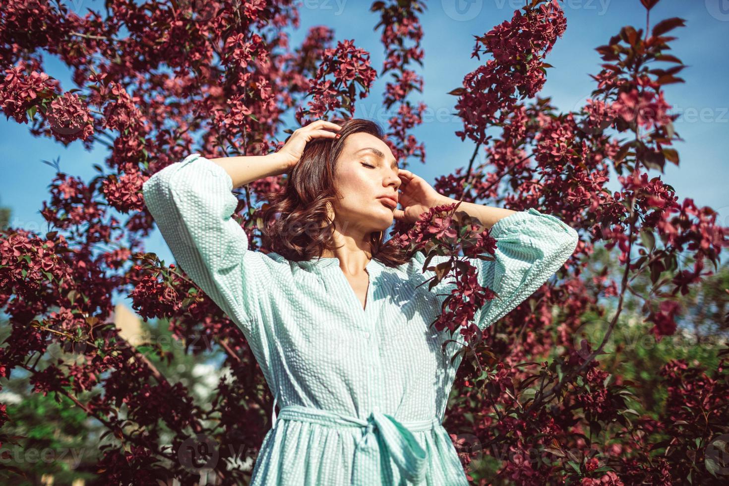 A young girl is standing in the park under a blossoming apple tree photo