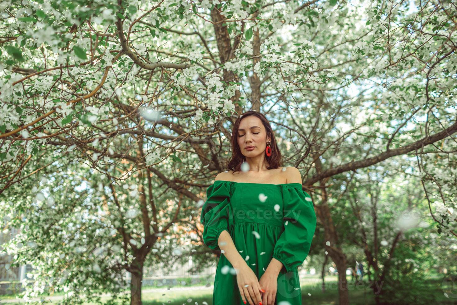 A young girl is standing in the park under a blossoming apple tree photo